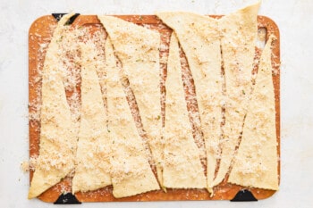 crescent rolls coated in cheese and seasoning salt on a wooden cutting board.