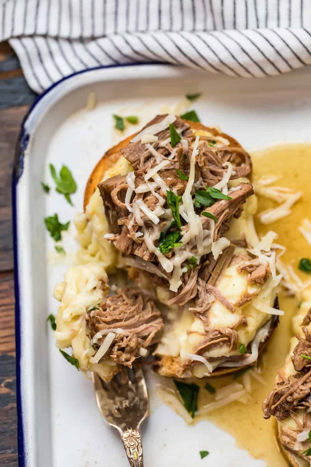 Open faced roast beef sandwich served atop creamy mashed potatoes smothered in savory gravy on a pristine white plate.