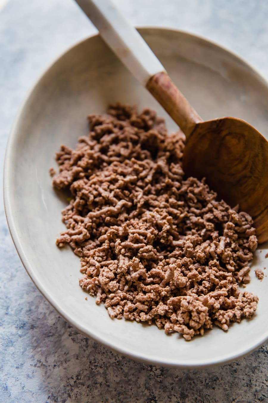 a serving plate of brown, boiled ground beef crumbles with a wooden serving spoon.