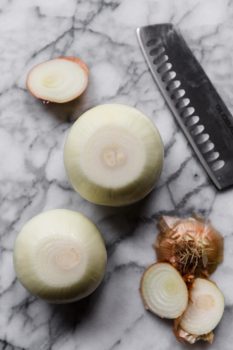 Step-by-step guide on cutting onions using a knife and marble table.