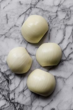 four white garlic cloves displayed on a marble surface.