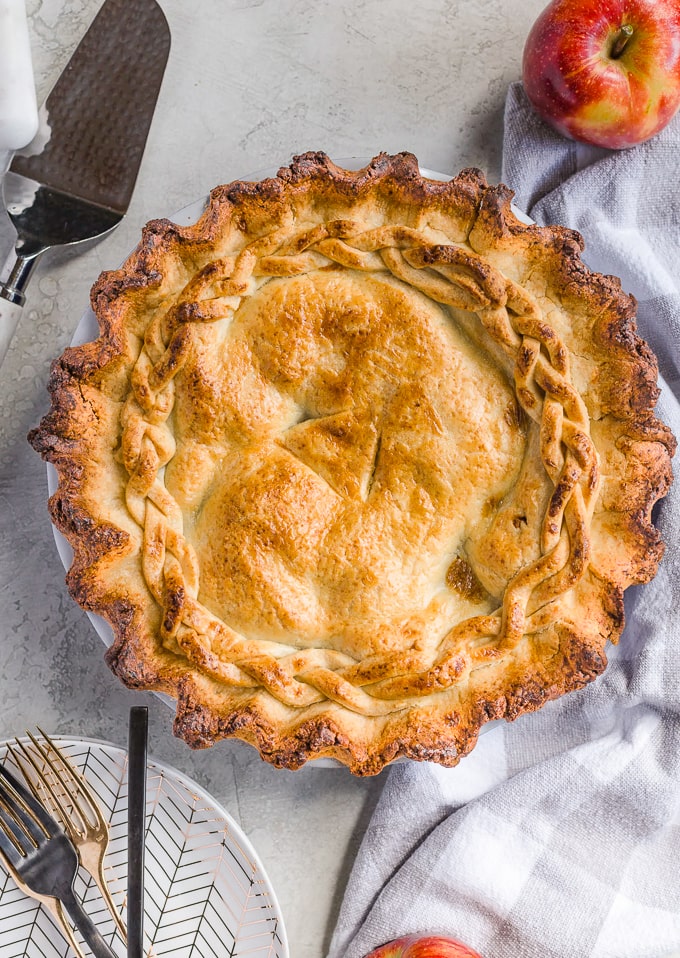 Homemade apple pie on a tabletop with plates and forks.