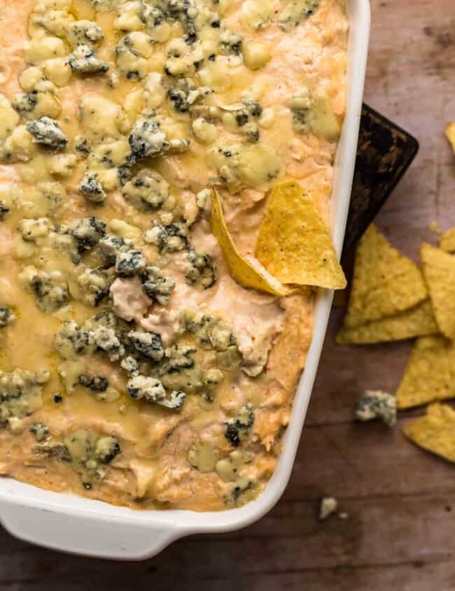 beer cheese buffalo chicken dip in a serving dish with a chip