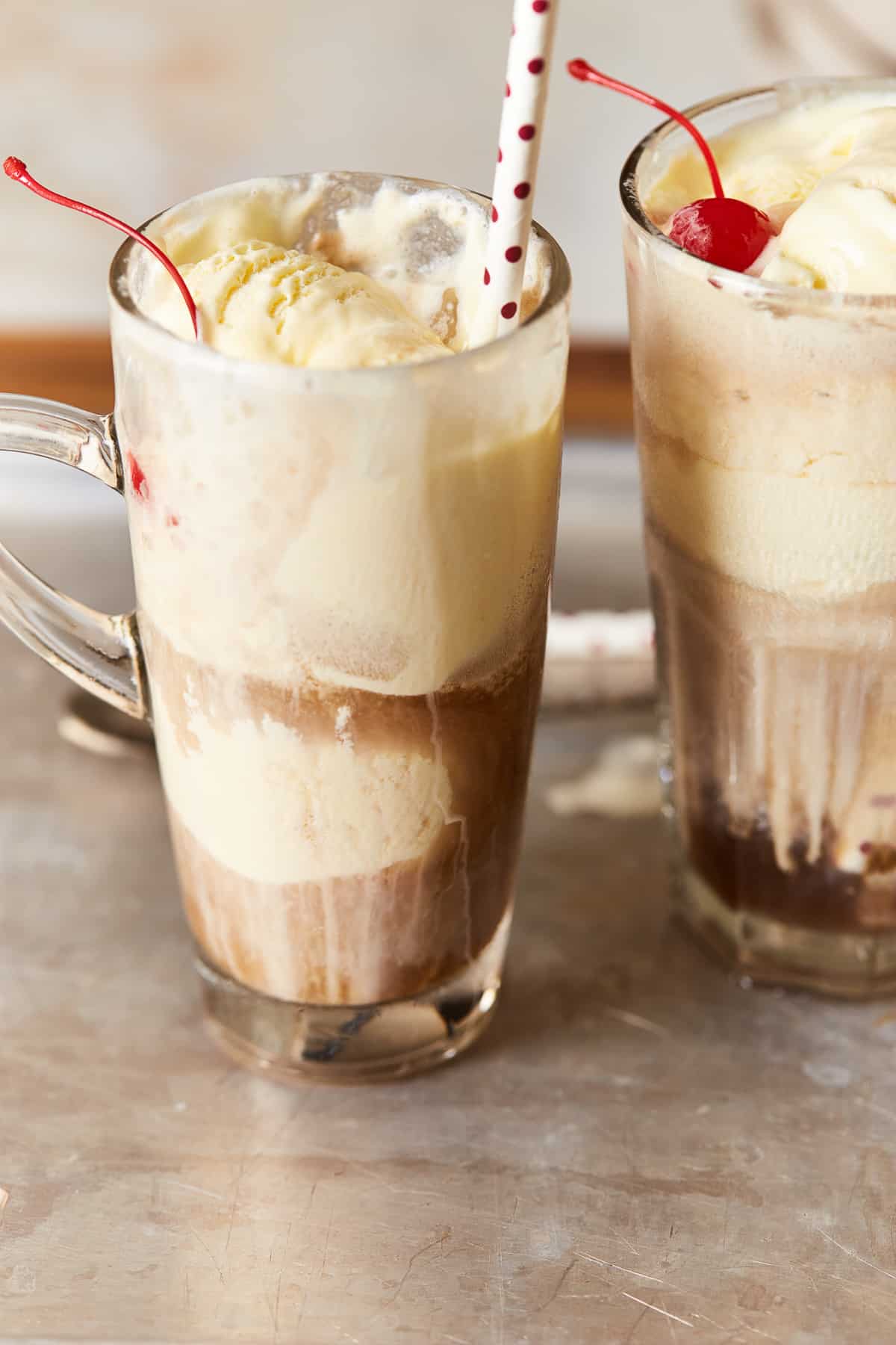 2 alcoholic root beer floats in tall clear glasses with handles with paper straws.