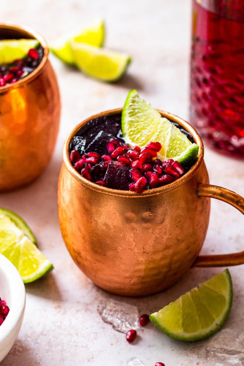 pomegranate moscow mules garnished with limes and pomegranate seeds