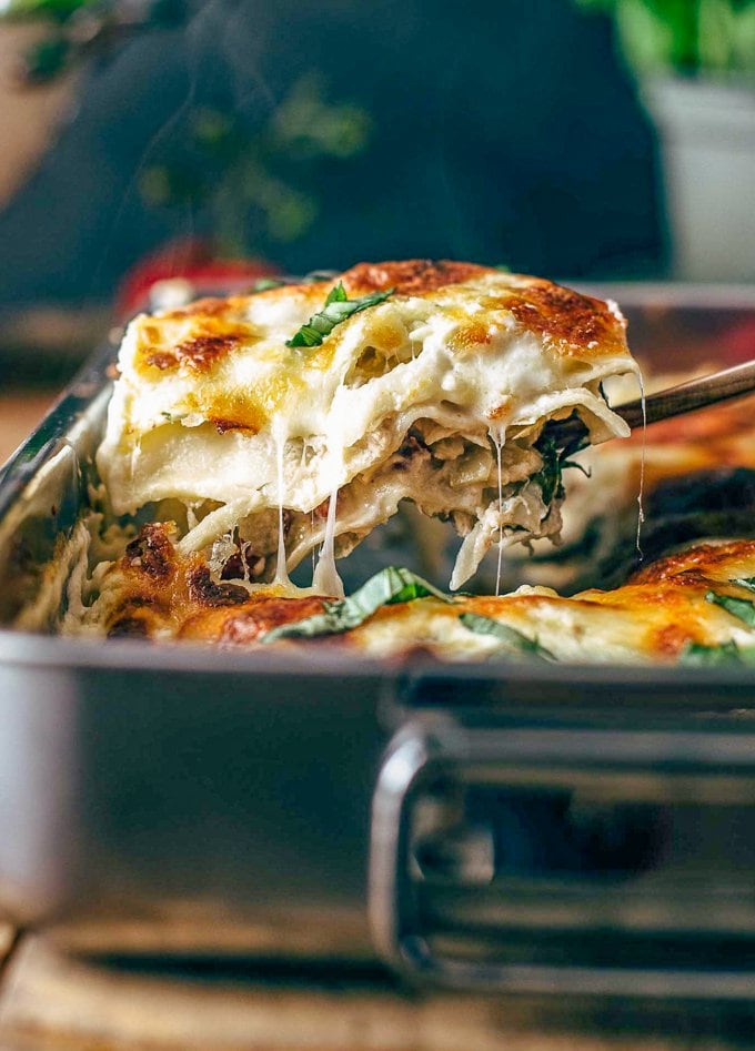 A white lasagna is being taken out of a baking dish.