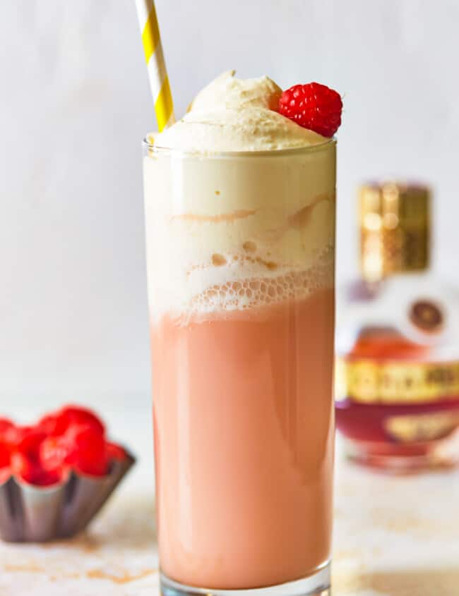 side view of raspberry italian cream soda in a tall glass topped with whipped cream, a raspberry, and a straw.