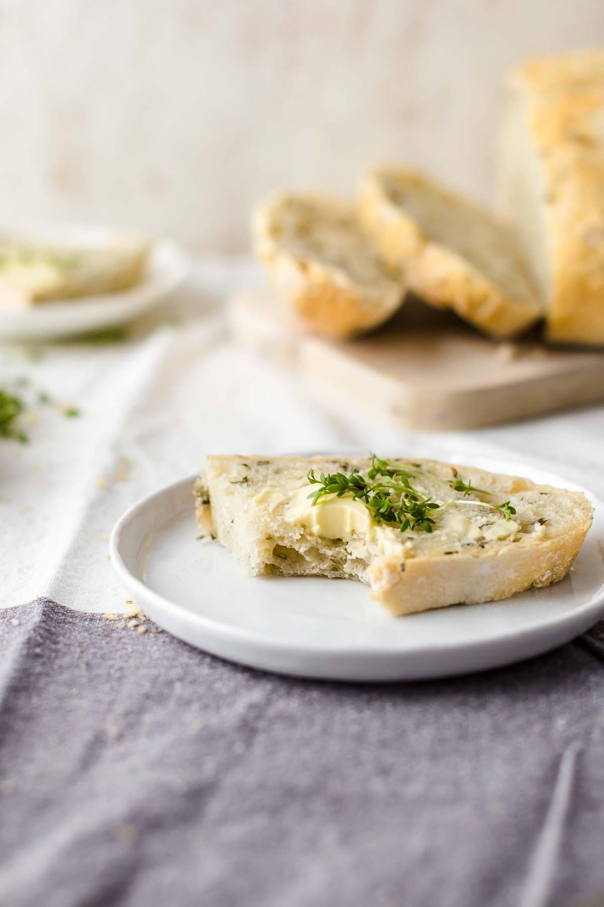 A slice of rosemary bread on a white plate with butter and thyme leaves.