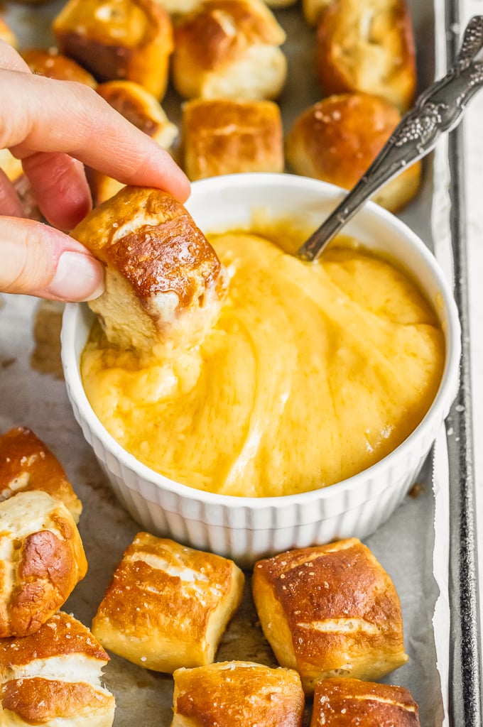 hand dipping pretzel bite into cheese dip