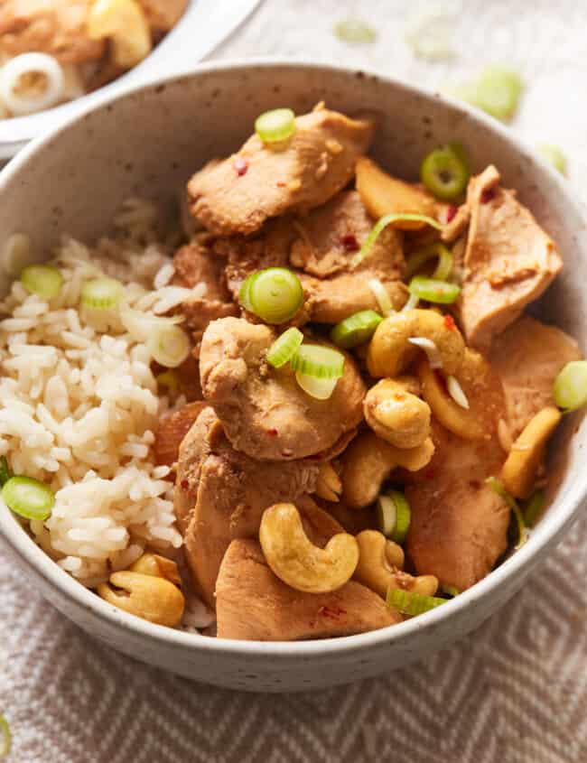 three-quarters view of crockpot cashew chicken in a tan bowl with rice.