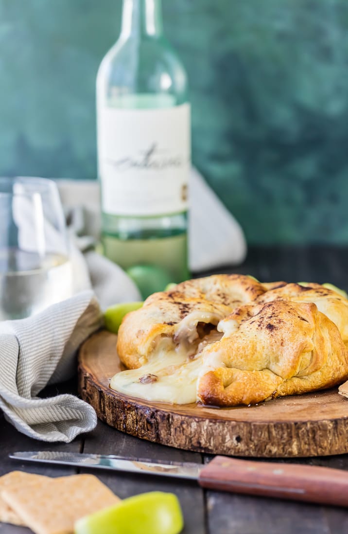 apple pie baked brie on wooden board with knife and wine bottle