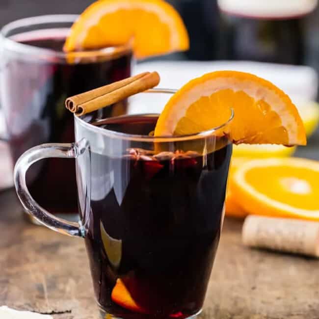 Two glasses of glühwein with orange slices and cinnamon sticks.