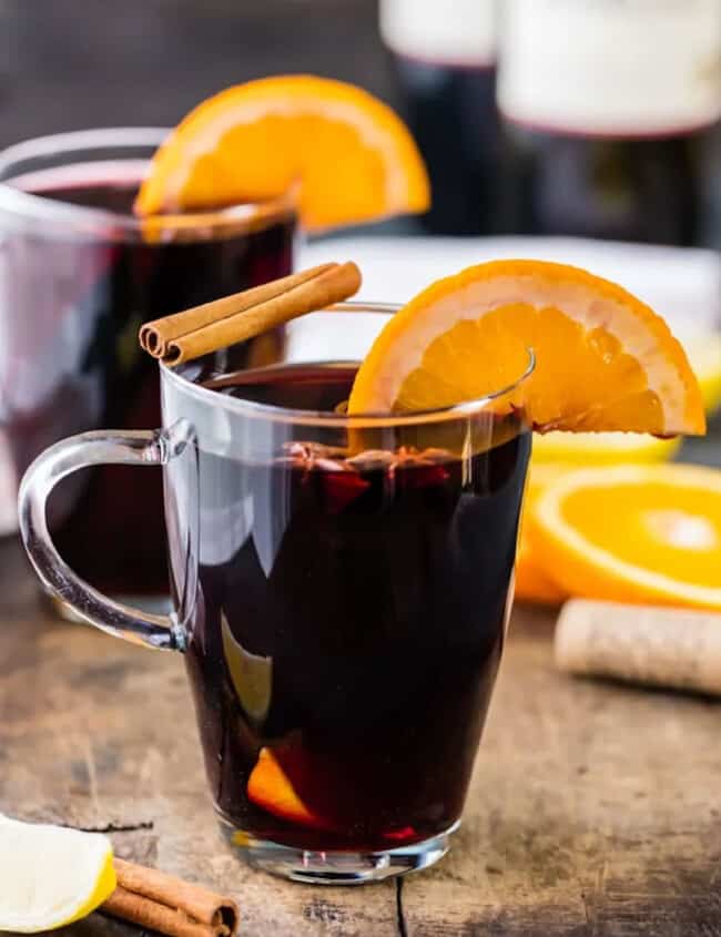 Two glasses of glühwein with orange slices and cinnamon sticks.