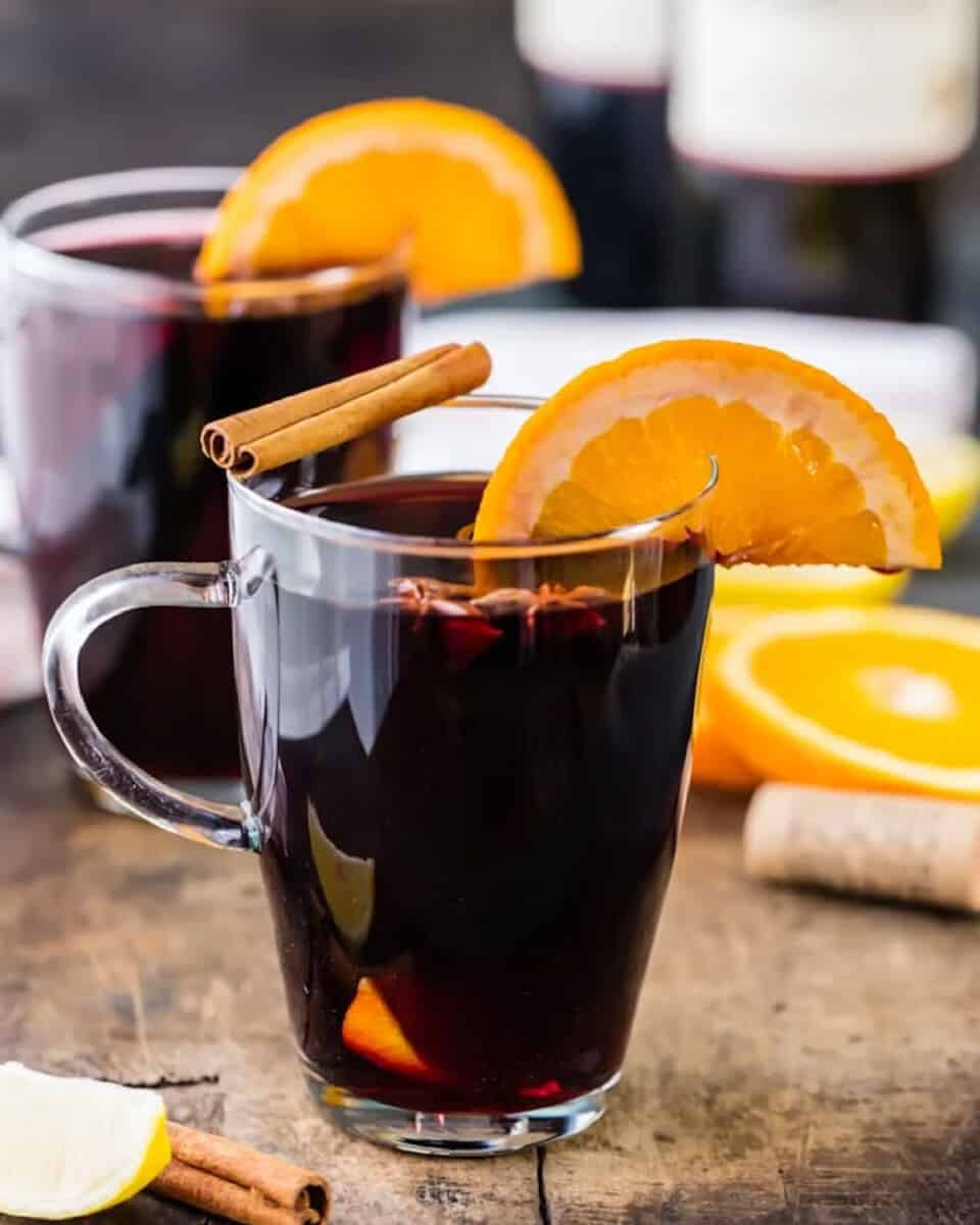 Two glasses of glühwein with orange slices and cinnamon sticks.