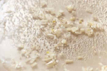 close up of chopped garlic and white wine cooking in a pan.