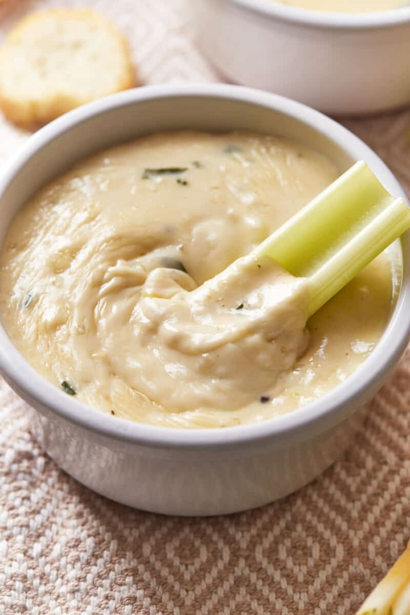 a piece of celery resting in a bowl of white wine fondue.