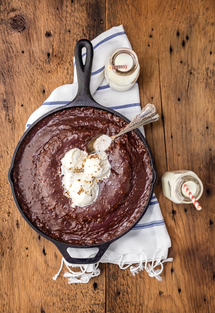 chocolate cake in a skillet next to two jars of milk