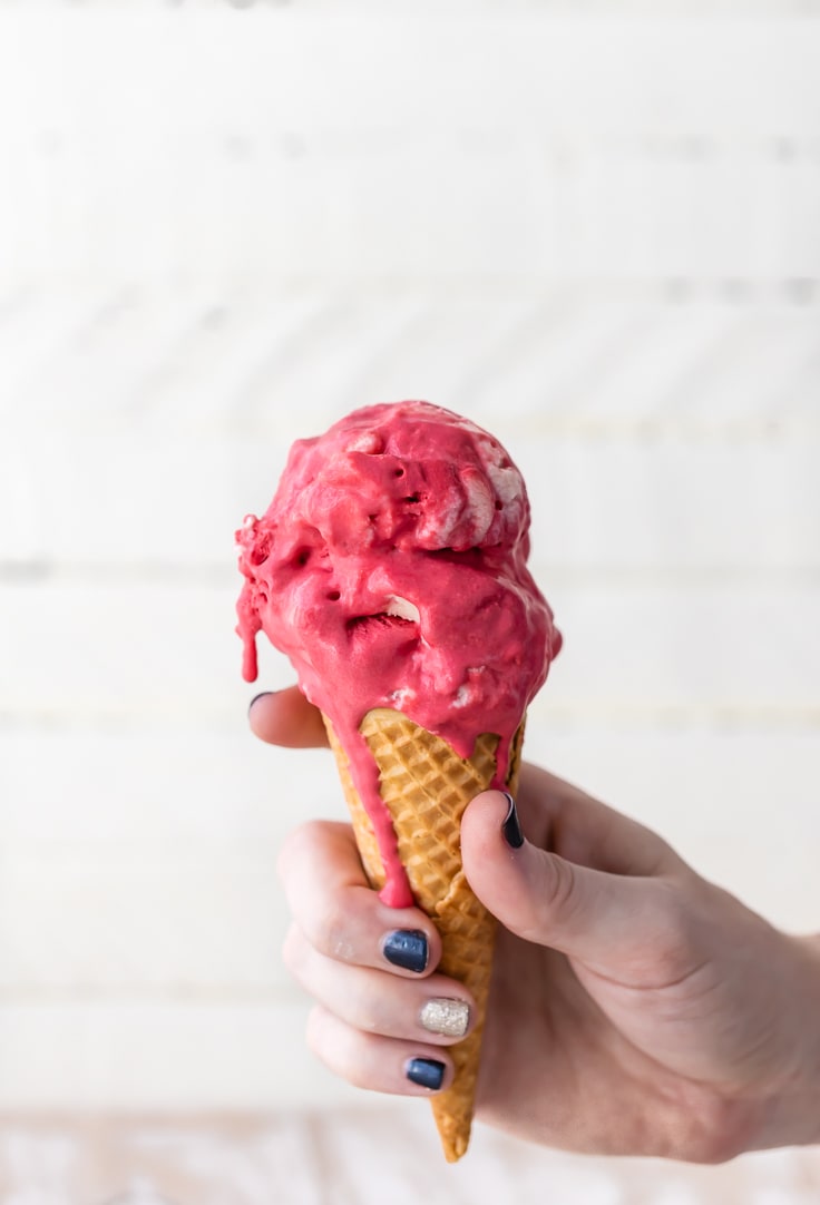 a hand holding an ice cream cone with red velvet ice cream dripping down the side