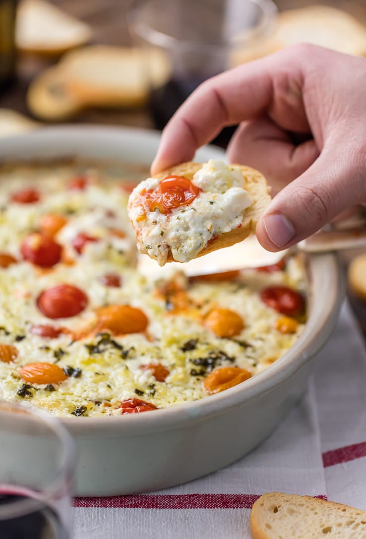 a hand holding a slice of bread topped with goat cheese dip