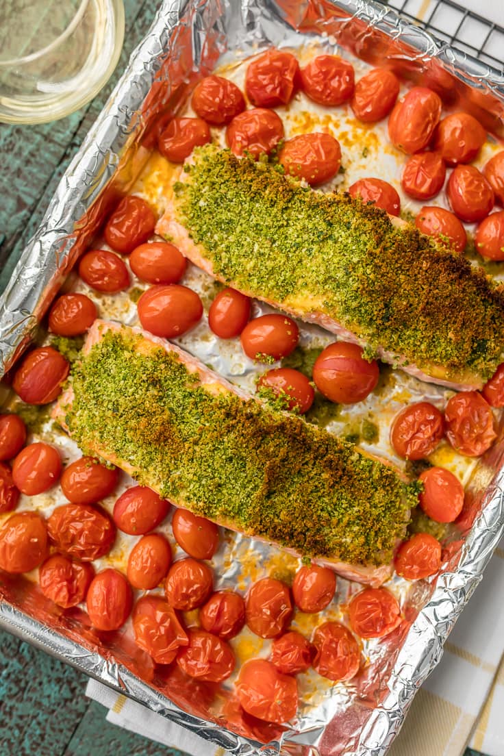 herb crusted salmon surrounded by cherry tomatoes on a baking sheet