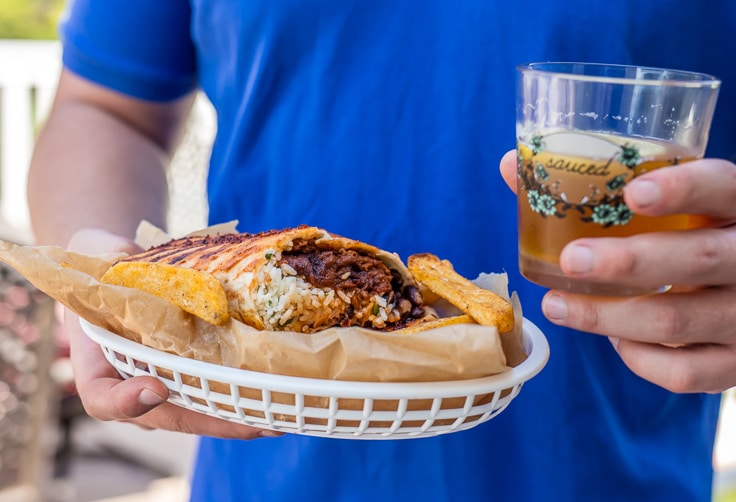 man holding a bbq burrito and a beer