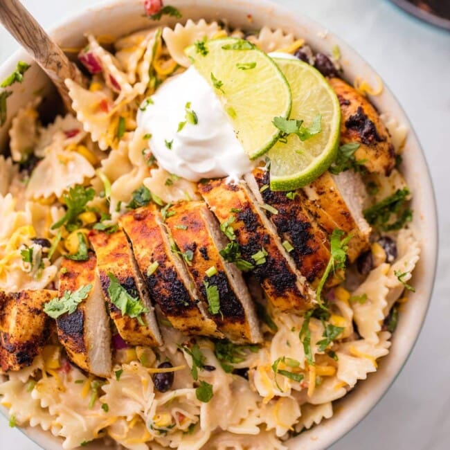 bowtie pasta in a bowl topped with sliced chicken, garnished with sour cream, lime, and parsley