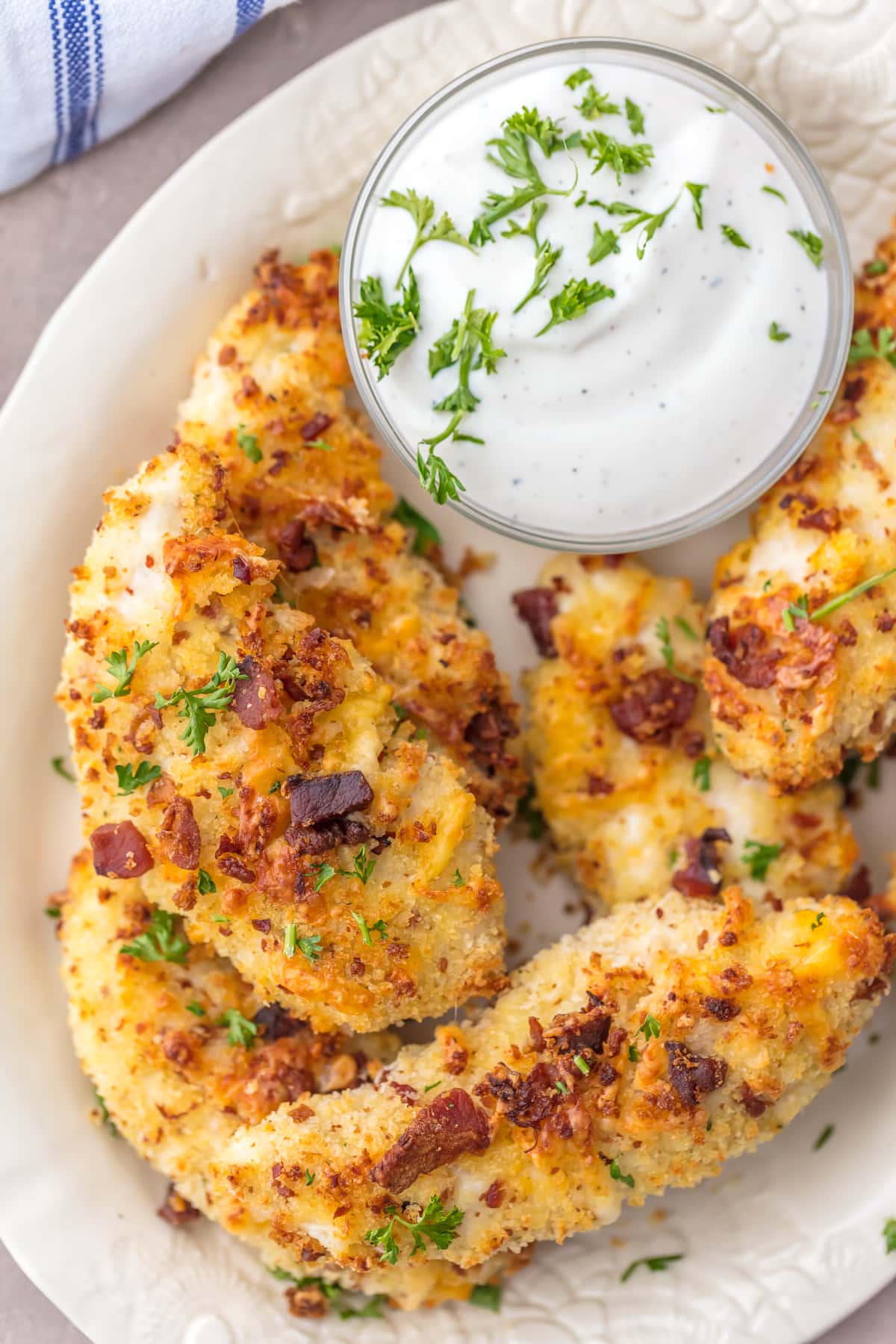 A plate of baked chicken strips with a bowl of ranch dipping sauce