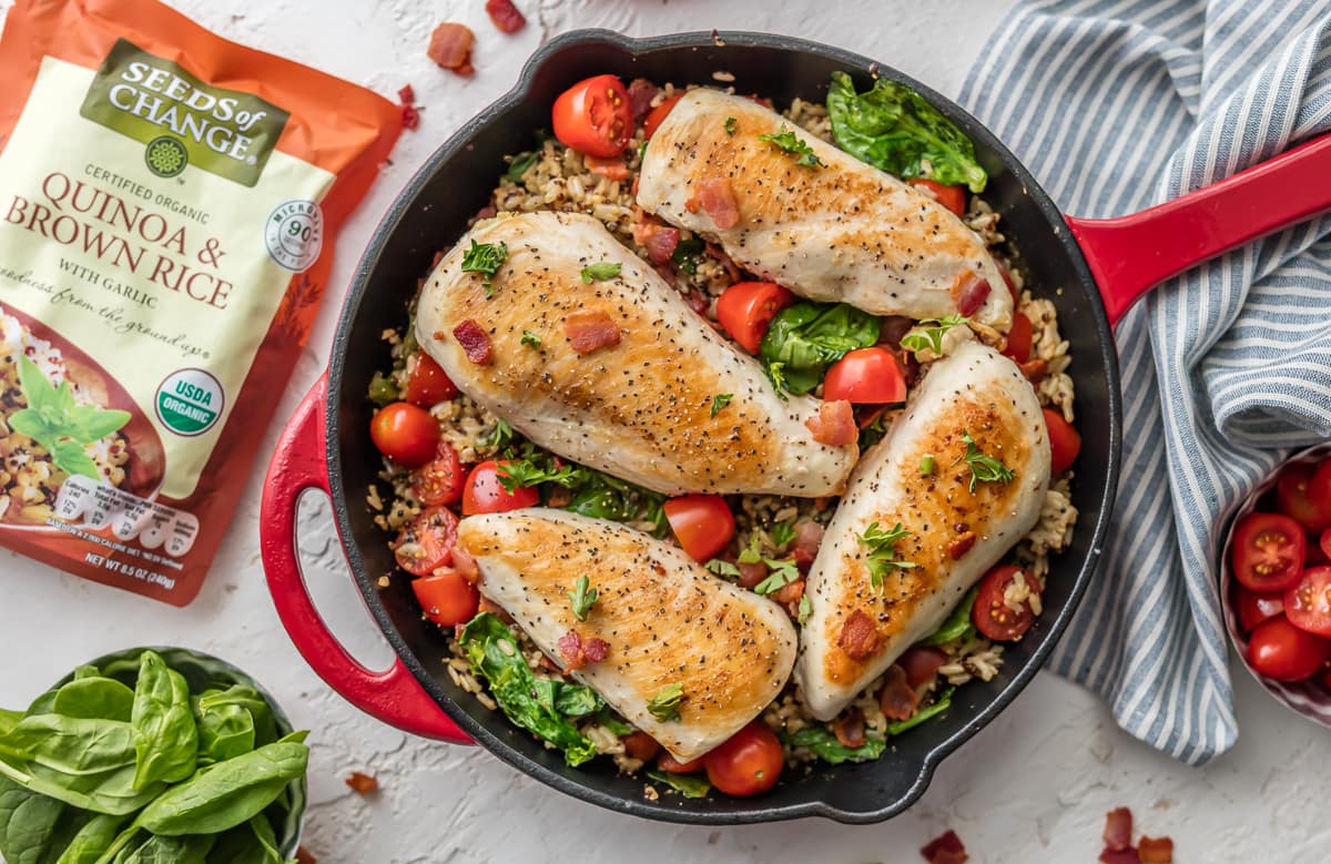 Red skillet filled with chicken breast, spinach, tomato, bacon, rice, and quinoa