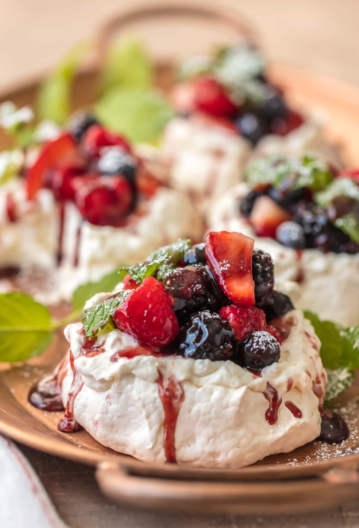 Mini Pavlova recipe topped with berries,sauce, and powdered sugar