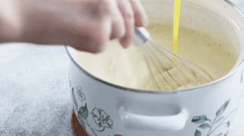 streaming eggs into a pot of milk with a whisk.