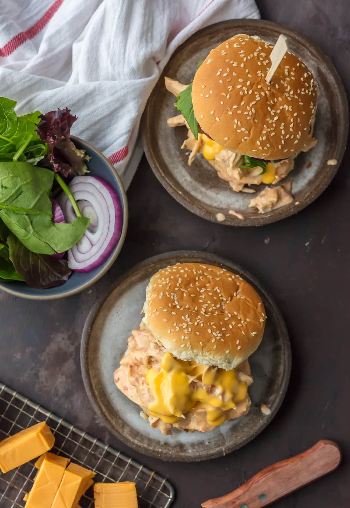 Two Chicken Rotel Dip Sandwiches on plates, next to a bowl of lettuce and onion