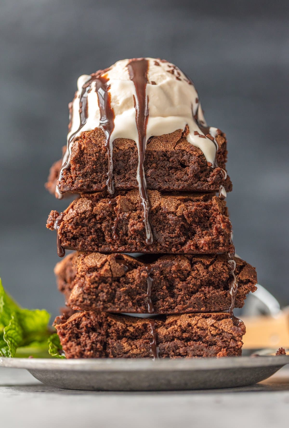 a stack 4 of homemade brownies topped with ice cream and chocolate sauce on a white plate.