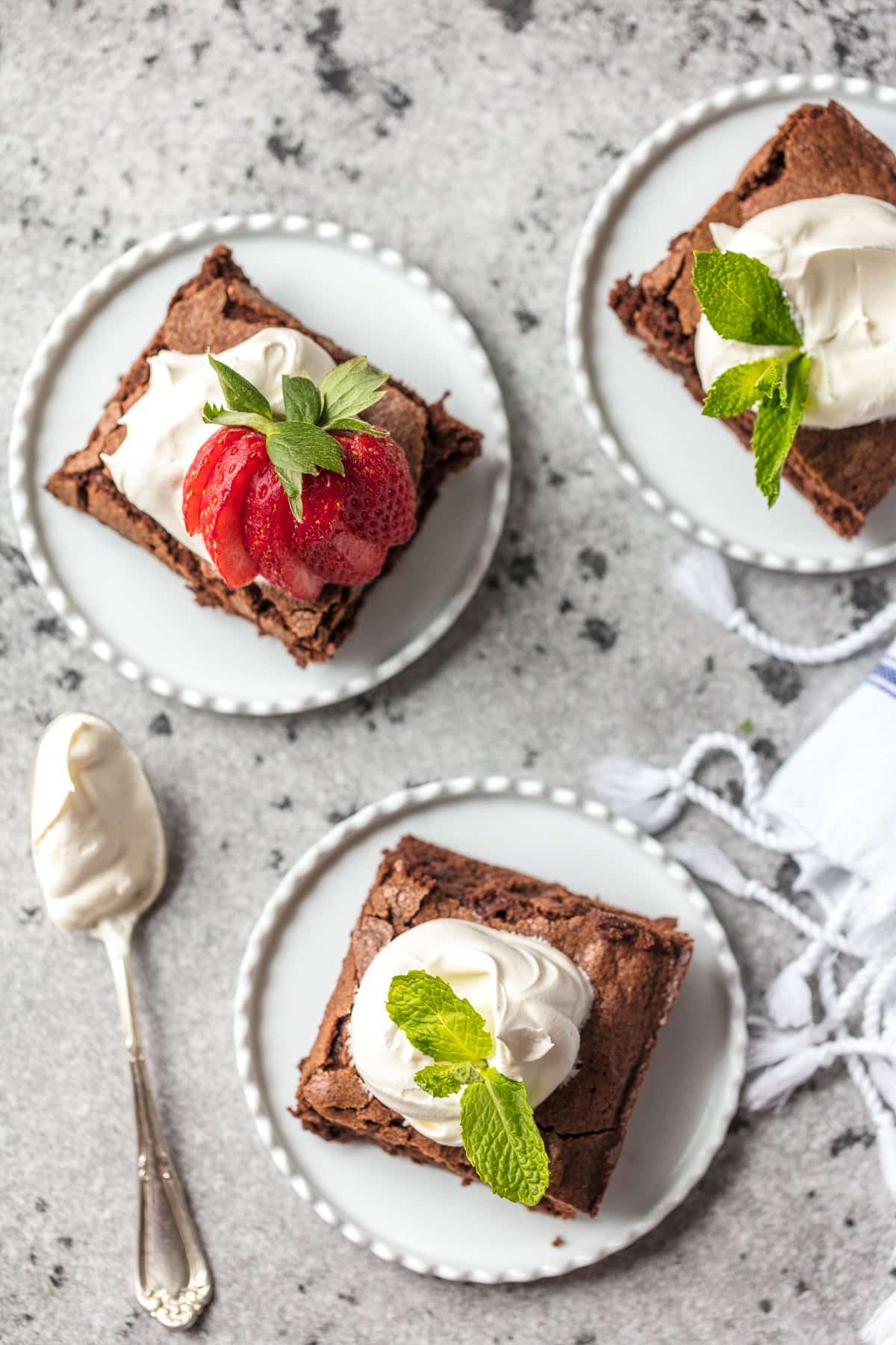 homemade brownies on white plates topped with whipped cream, berries, and mint.