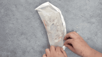 Hands folding salmon in parchment paper.