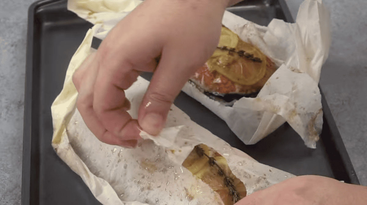 hand ripping open a parchment paper pocket on a baking sheet.