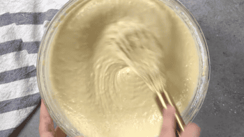 stirring pancake batter in a glass bowl with a whisk.