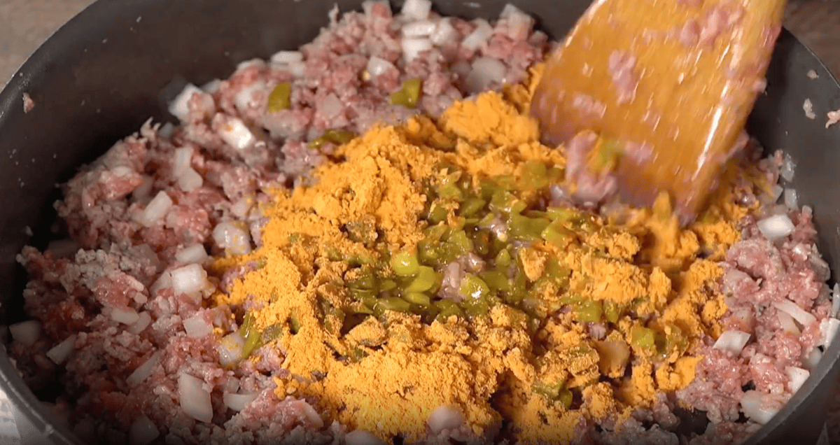 adding taco seasoning and green chiles to pork and onions in a pan with a wooden spoon.