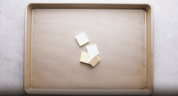 A piece of butter on a baking sheet, used to make flavorful parmesan potato wedges.