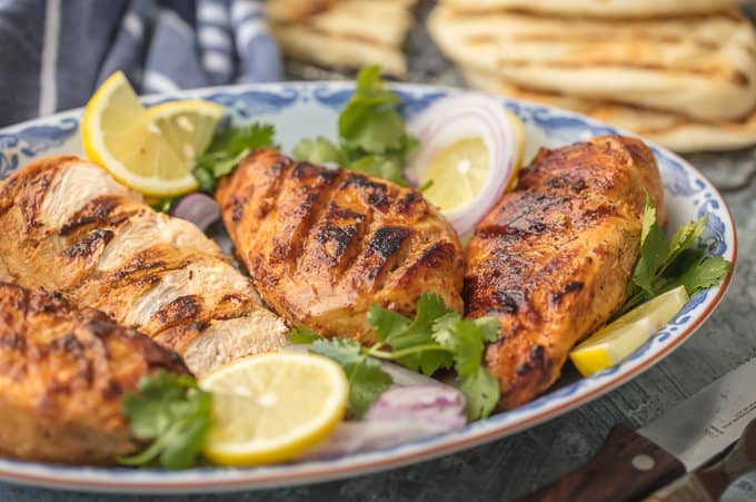 a platter of tandoori chicken with cilantro, lemon, and onion