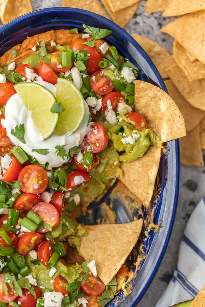 This Layered Bean Dip Recipe is one of our favorite ways to tailgate! Guacamole Bean Dip has layers of guacamole, spicy refried beans, tomatoes, onions, and cheese. This Mexican Bean Dip is SO delicious and made in minutes! It doesn't get better than Layered Bean Dip for any and every celebration!