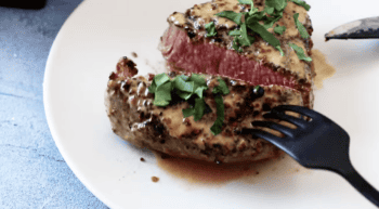 A succulent peppercorn steak, perfectly cooked to perfection, is served on a pristine plate with a shiny fork.