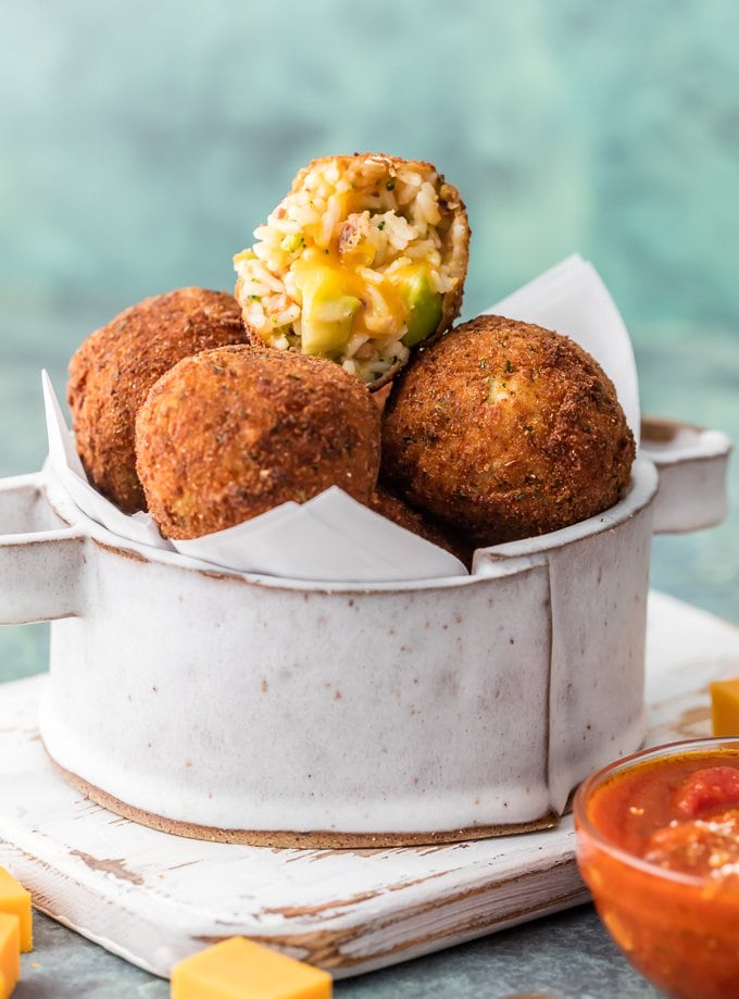 A bowl full of rice balls, one pulled apart to show rice, broccoli, and cheese inside