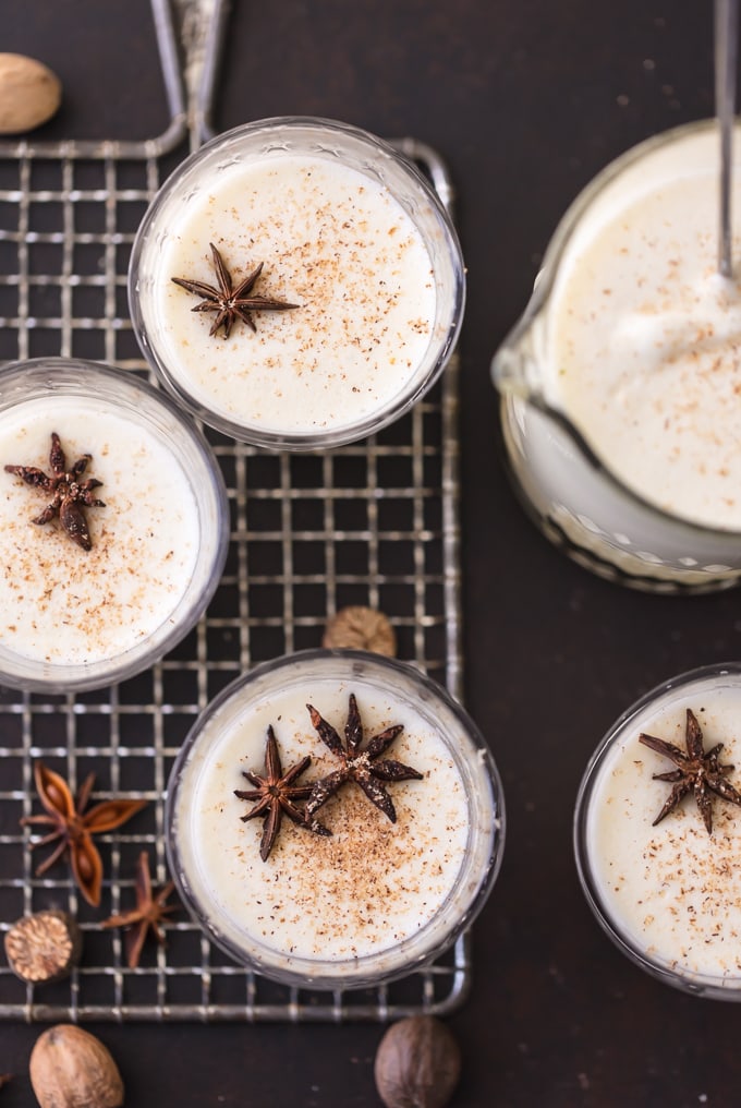 beautiful overhead image looking down on 4 glasses and a pitcher full of homemade traditional eggnog. Glasses are garnished with pieces of star anise and ground nutmeg