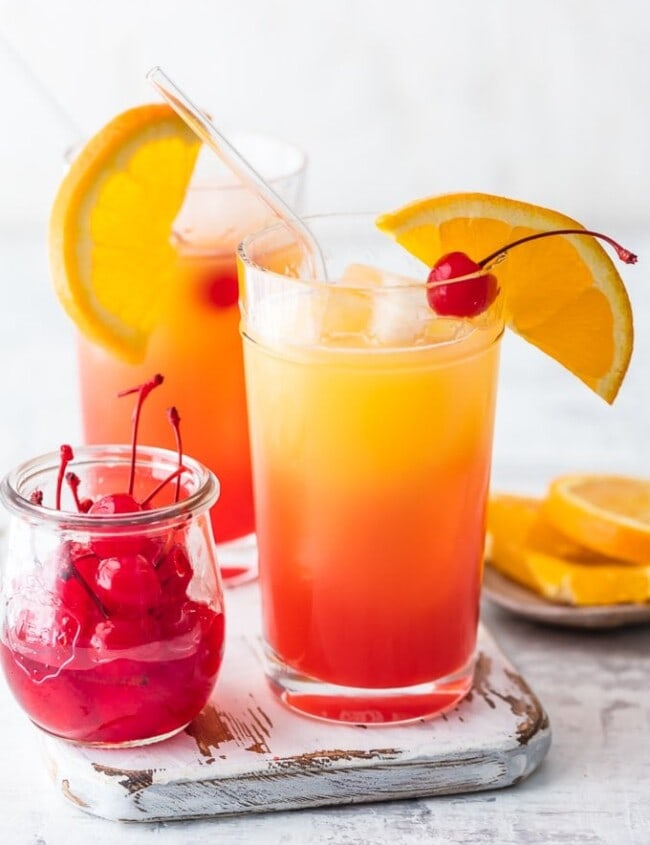 cocktails in glasses next to cherries and oranges