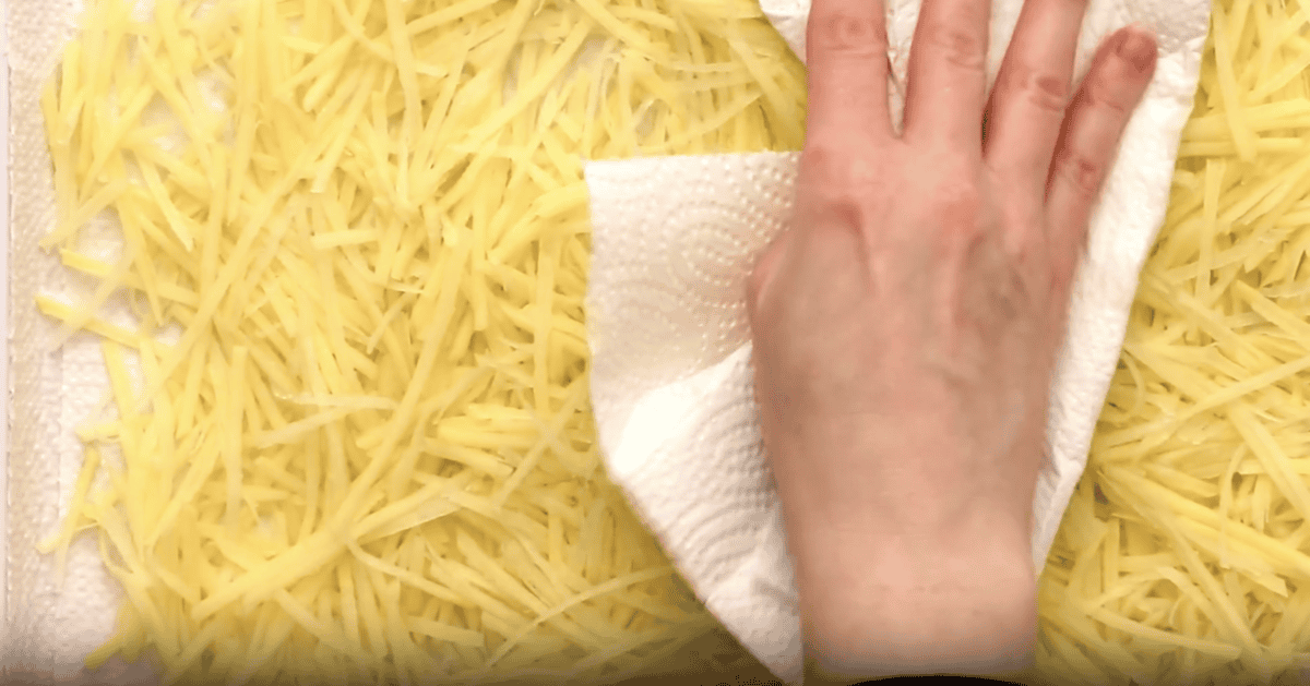 patting julienned potatoes dry on a paper towel-lined baking sheet.