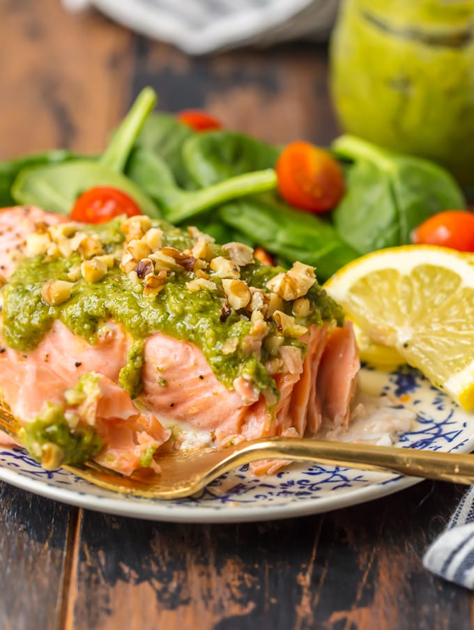 Baked Salmon with Basil Walnut Pesto is our favorite simple yet elegant seafood dinner. This Pesto Salmon Recipe is bursting with flavor and good fat. The tender flakey salmon is basted in butter, white wine, and lemon juice before baking and then topped with an amazing nutty and rich Basil Walnut Pesto. Best Salmon Recipe ever!