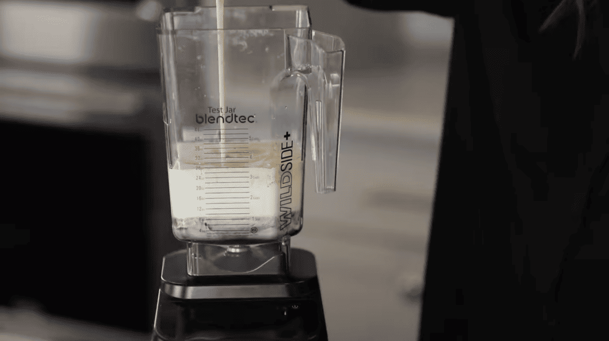 A woman pouring homemade Irish cream into a blender.