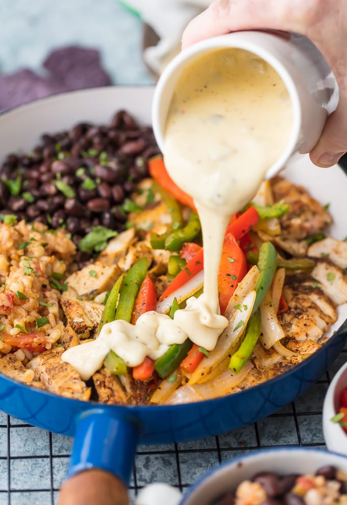 pouring cheese over a skillet of chicken and vegetables