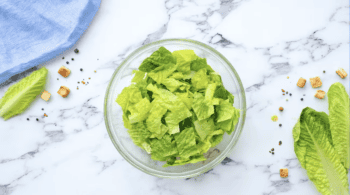 A caesar salad with lettuce in a glass bowl on a marble table, featuring caesar salad dressing.