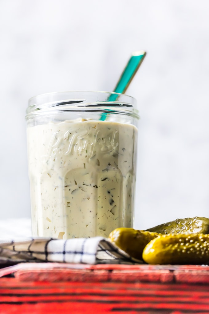 Tartar sauce in a glass jar, next to 3 dill pickles